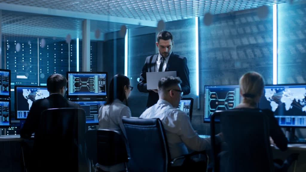 corma- A group of people sitting at desks, dedicated to corporate security, with monitors in front of them.